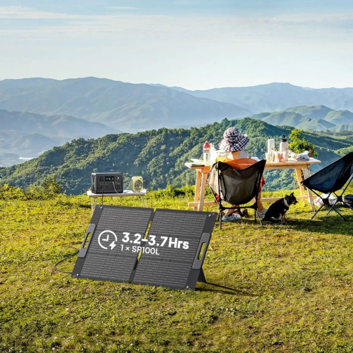 Person sitting at a table with a scenic view of mountains, BLUETTI SP100L Solar Panel  on the ground.