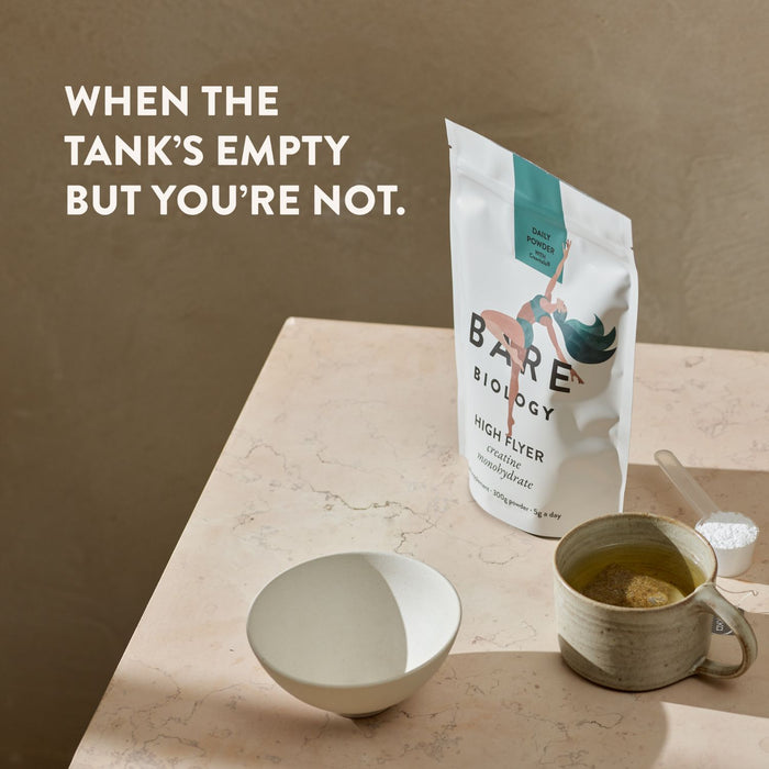 Bare Biology Creatine Pouch on a neutral marble effect surface next to a scoop with powder in it a mug of tea in a beautiful ceramic mug arranged next to a white porcelain bowl.