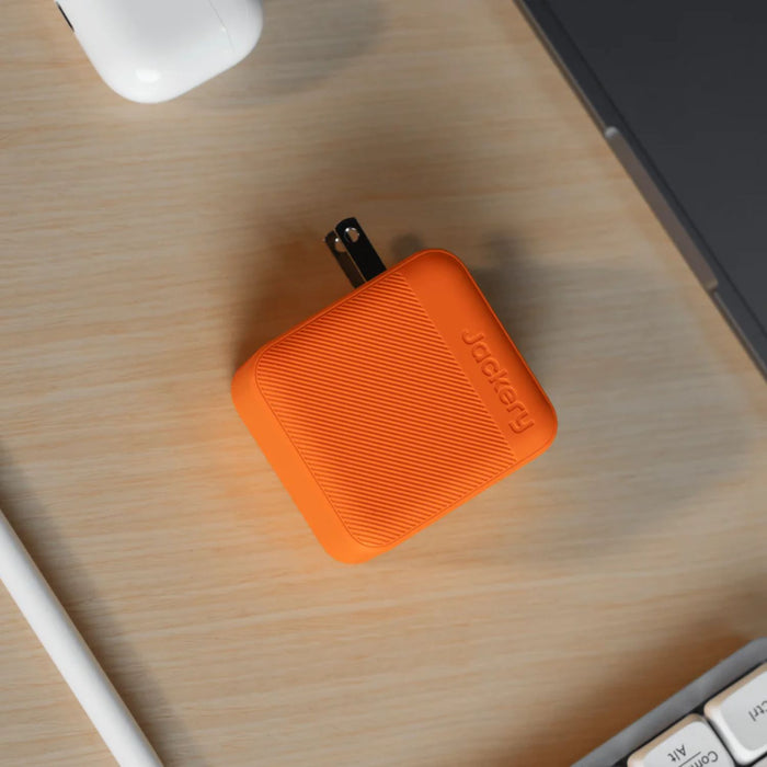 Jackery 102W GaN 3-Port Fast Charger on a wooden desk with computer equipment.
