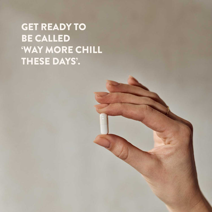 Hand holding a small white magnesium tablet with text on a plain background that reads get ready to be called 'way more chill these days'.